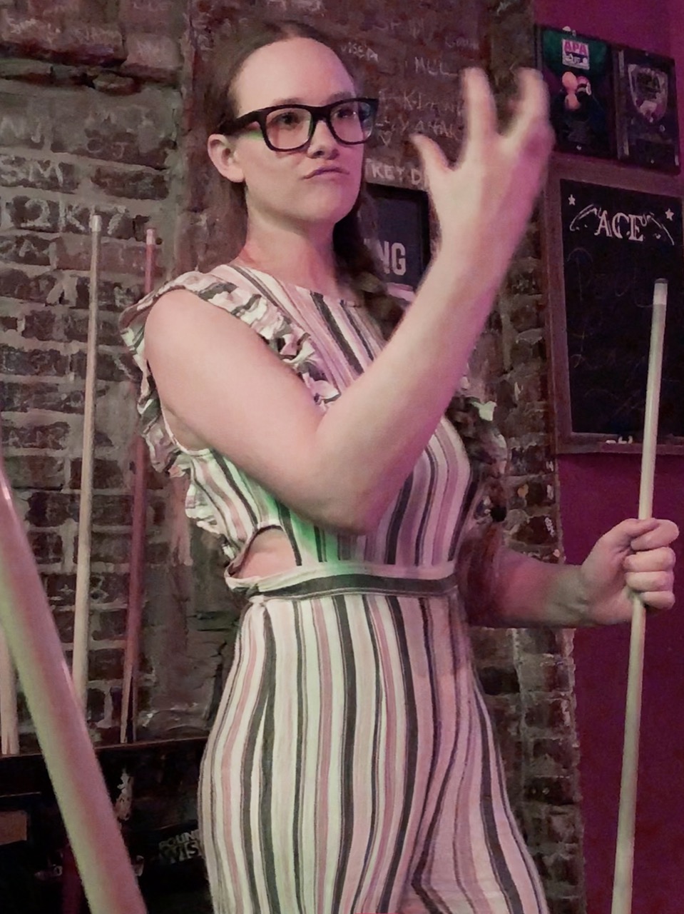 A picture of Hannah holding a pool stick in one hand and the other hand gesturing.